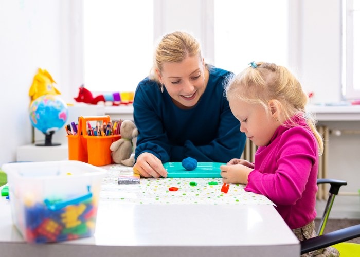 Toddler girl in child occupational therapy session doing sensory playful exercises with her therapist.